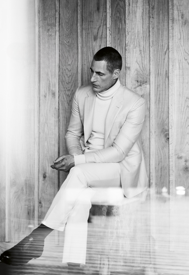 Black and white picture of model wearing turtleneck and Zegna suit sitting down