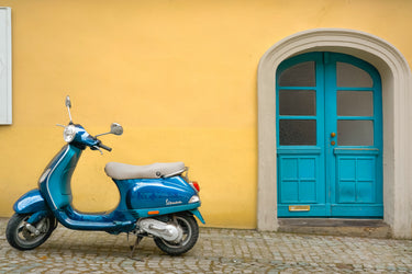 A blue moped is parked beside a blue door on an Italian street in front of a mustard yellow wall
