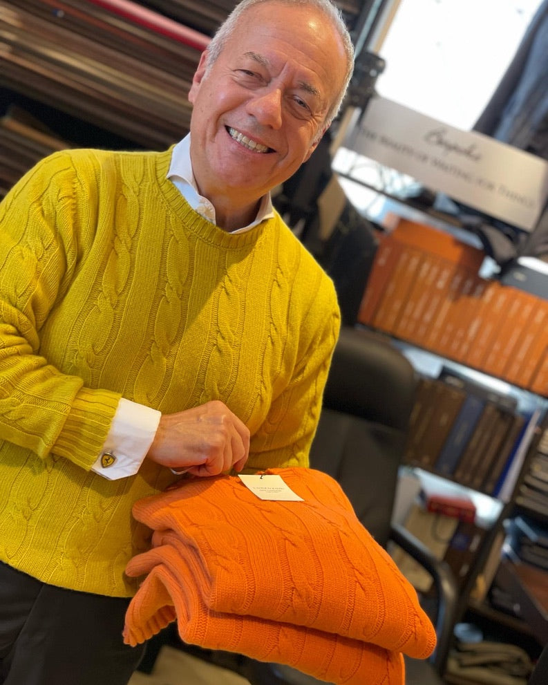 John De Laurentiis wearing yellow Lorenzoni cashmere sweater holding two of the same sweaters in orange